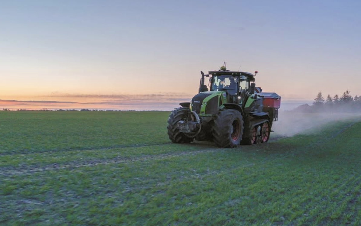 Claas Axion ar mēslojuma izkliedētāju vakara gaismā